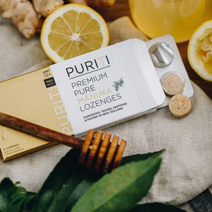Puriti Manuka Honey Lozenges UMF 12+ box of 8 lozenges, 2 lozenges displayed out of the box on a cloth next to a honey dipper