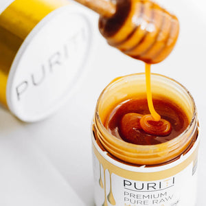 Puriti Premium Raw Manuka Honey Jar with the lid off, honey dipper hovering above the top of the jar with Manuka drizzling