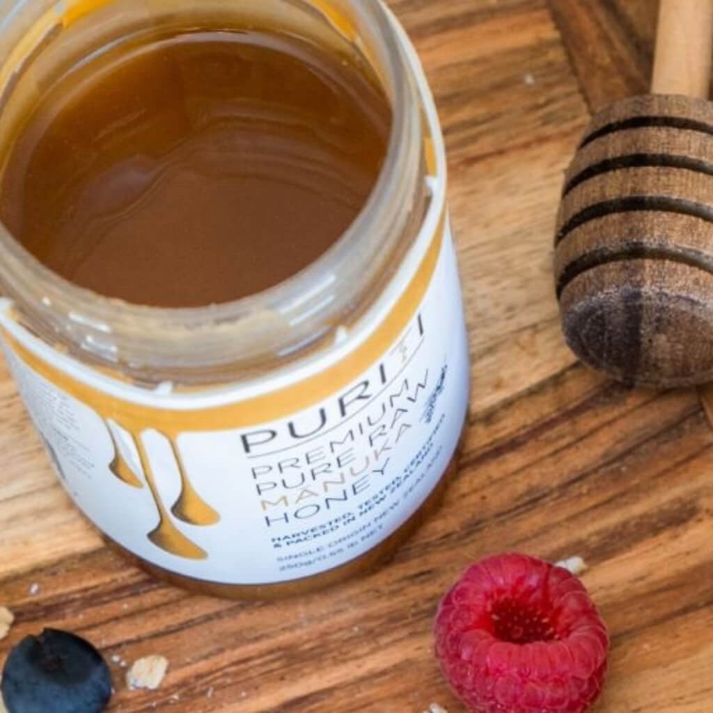 Genuine Manuka Honey Jar open top beside a honey dipper on a wooden cutting board