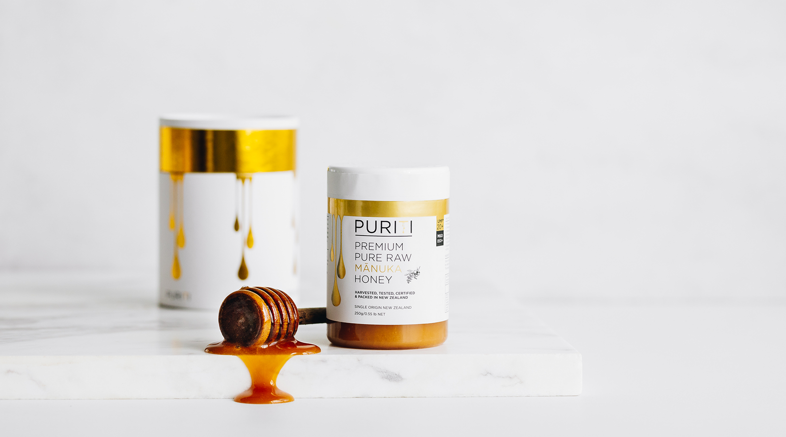 Genuine New Zealand Manuka Honey UMF 20+ on a white chopping board with honey dipper and Manuka honey drizzled along the front