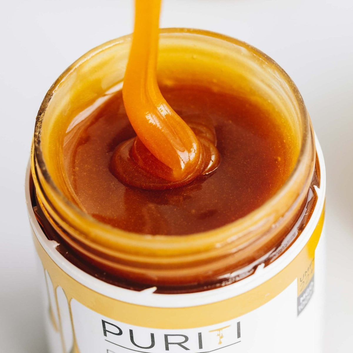 Puriti Premium Manuka Honey Jar with the lid off, Premium Manuka being drizzled into the jar from above